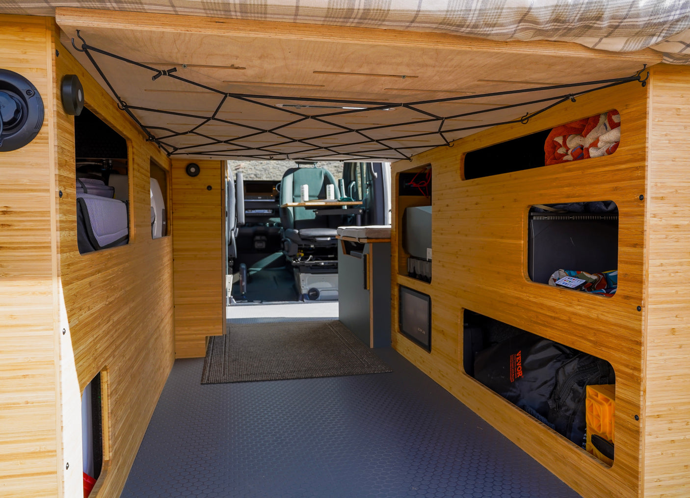 Inside an rv rental camper van: warm bamboo interior with practical storage, a flexible ceiling net, and a patterned floor.