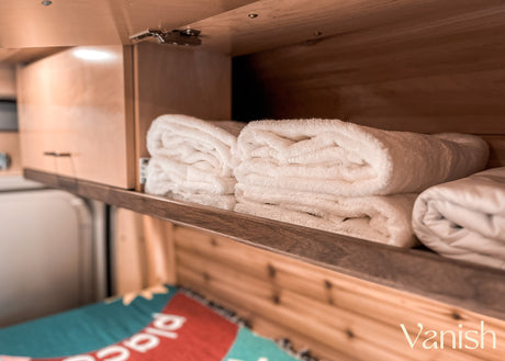 RV rental interior: Cozy storage shelf with folded white towels and linens, part of a colorful bed.