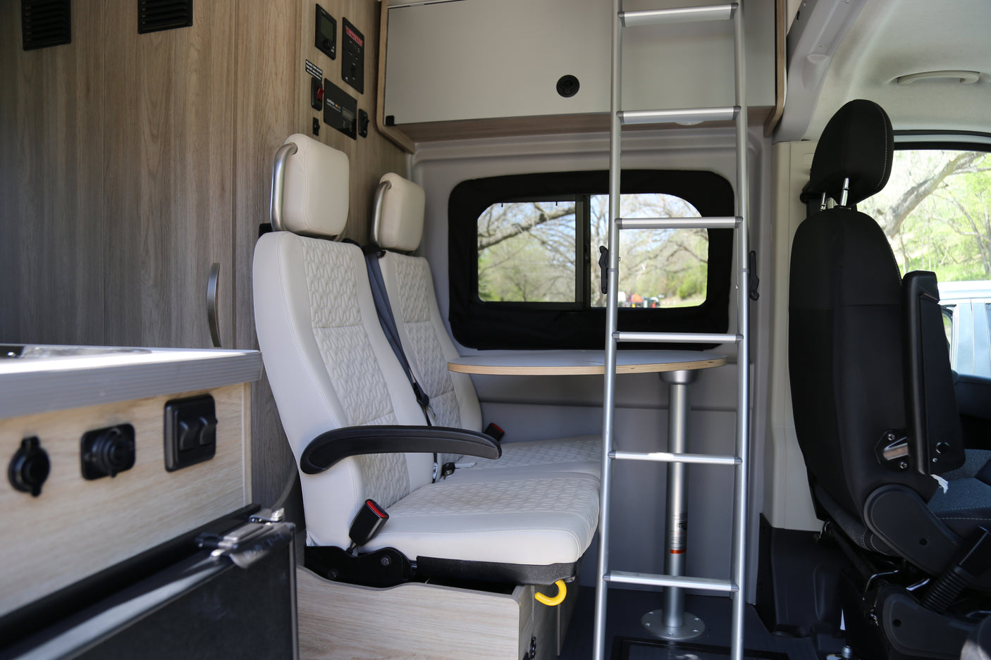 Inside an RV rental: light seats, table, and ladder for upper bunk access. Functional and ready for adventure.