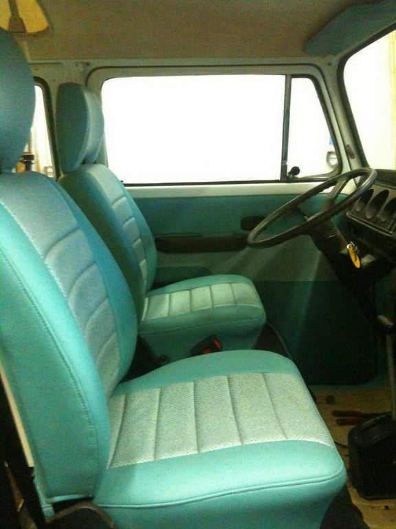 Inside this RV rental: bright, clean front cabin with two-tone teal & grey upholstered seats and steering wheel.