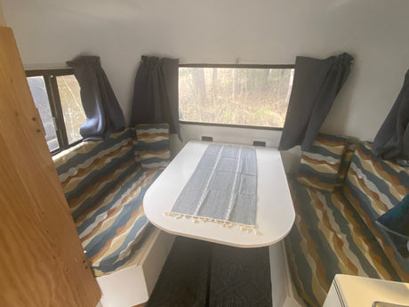 Cozy rv rental interior with a dining table, patterned cushions, and nature views from the windows.