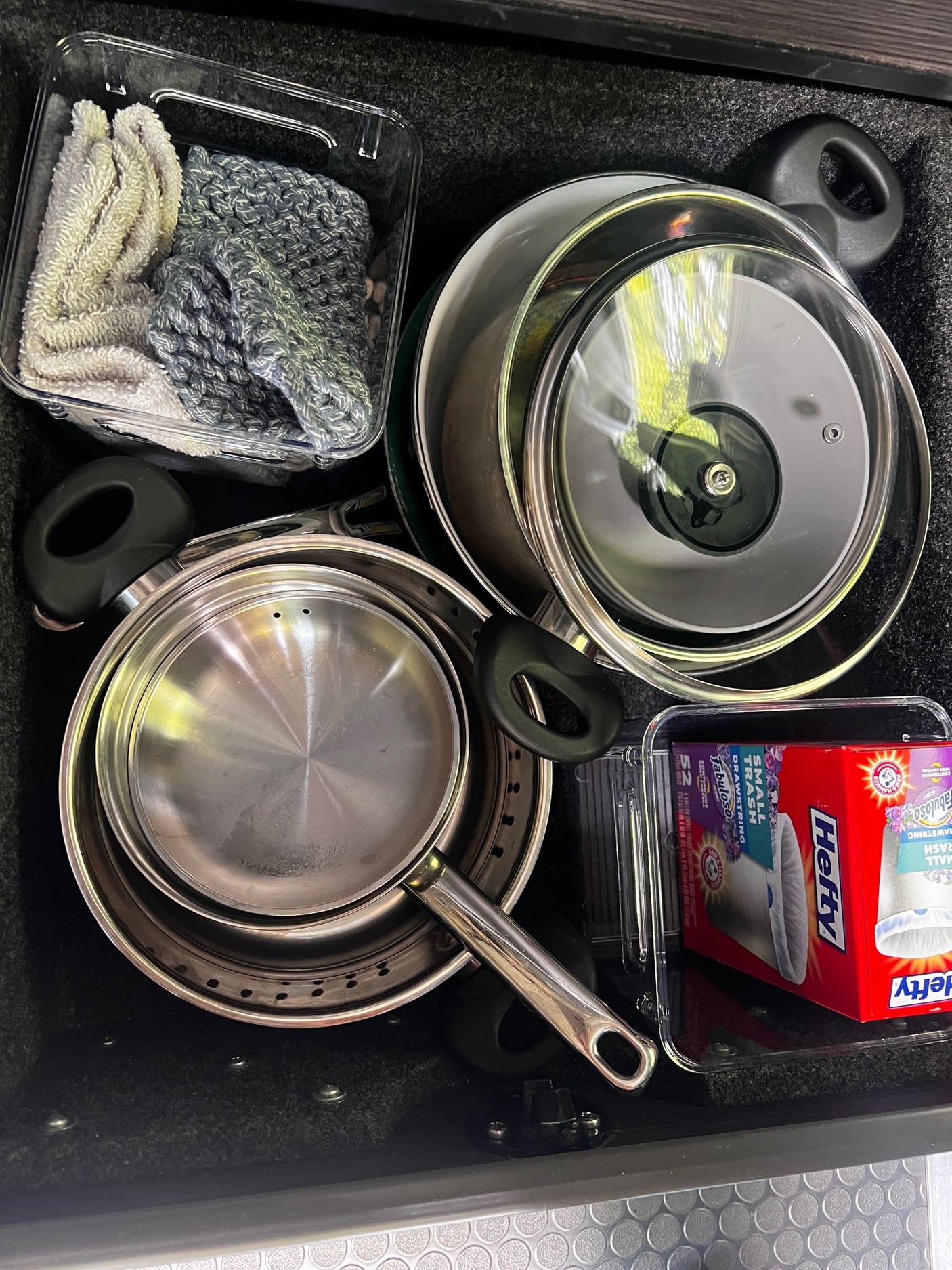 RV rental kitchen drawer: nested pots, pans, lids, and essentials like cloths & trash bags for travel.