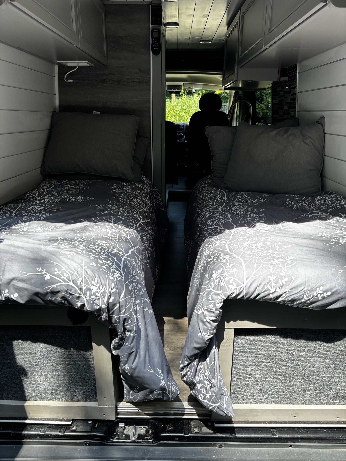 RV rental camper van interior with two comfortable single beds, grey patterned bedding, and narrow aisle leading to the front.