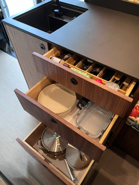 Organized RV rental kitchen with open drawers revealing cutlery, plates, and pots for efficient travel storage.
