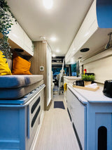 Comfortable RV rental interior with a modern design, featuring a compact kitchen, cozy seating/bed, and bright ambient lighting.