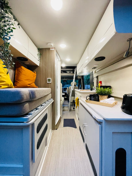 Comfortable RV rental interior with a modern design, featuring a compact kitchen, cozy seating/bed, and bright ambient lighting.