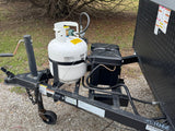  secured on the trailer frame. Provides essential gas for your trip.|RV rental's open exterior storage shows a neatly packed folding table and plastic-wrapped mattress on a laminate floor.|RV rental travel trailer's front area