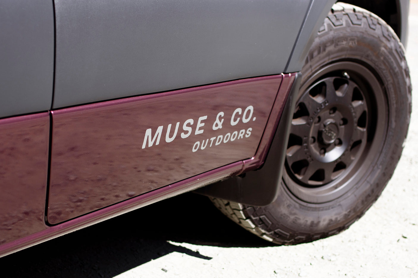 Side of a two-toned RV rental van with "MUSE & CO. OUTDOORS" branding and off-road tire.