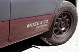 Side of a two-toned RV rental van with "MUSE & CO. OUTDOORS" branding and off-road tire.