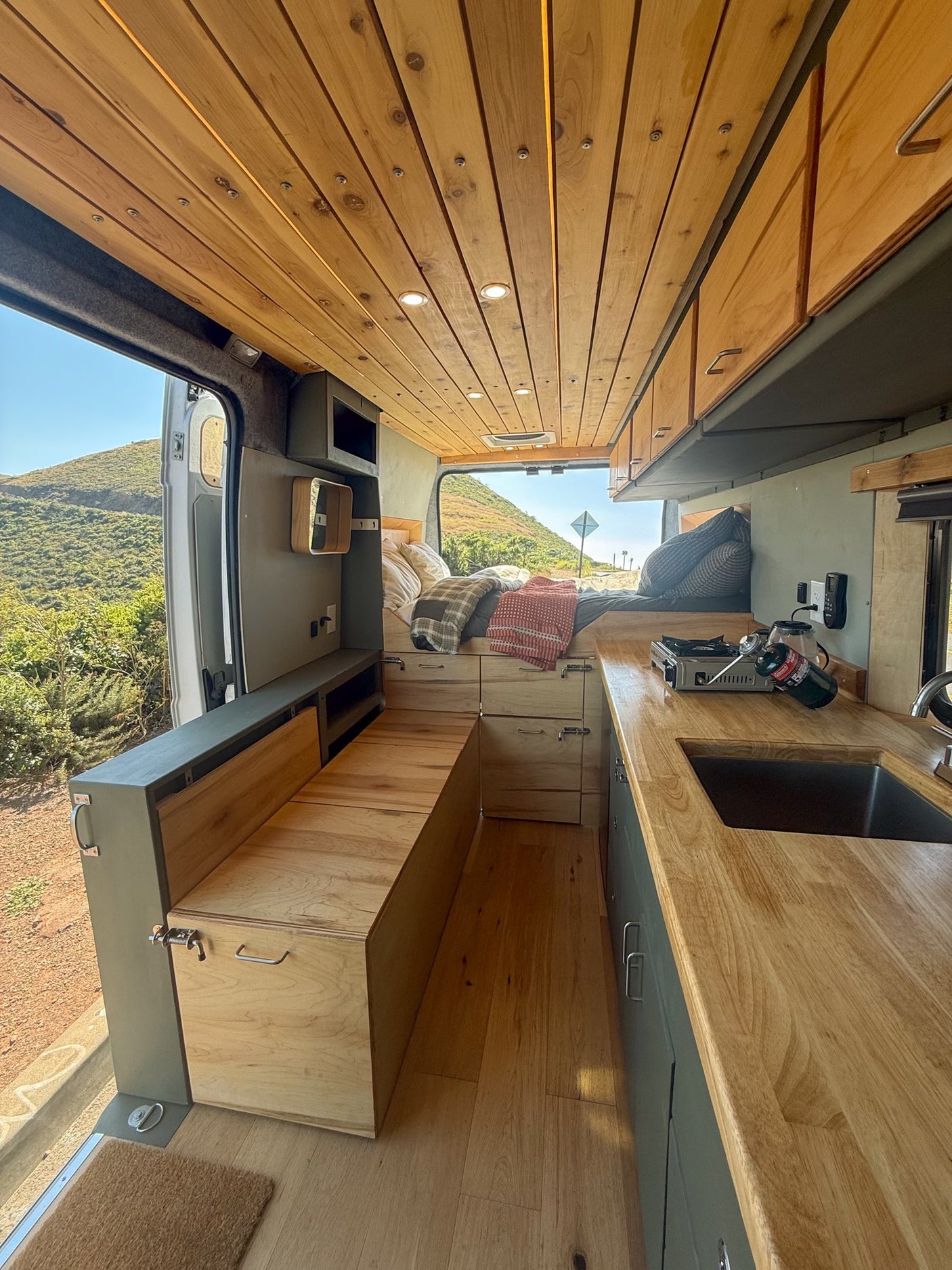Well-appointed camper van interior with wood ceiling & floors, kitchen, bed, & storage, ideal for an RV rental adventure.