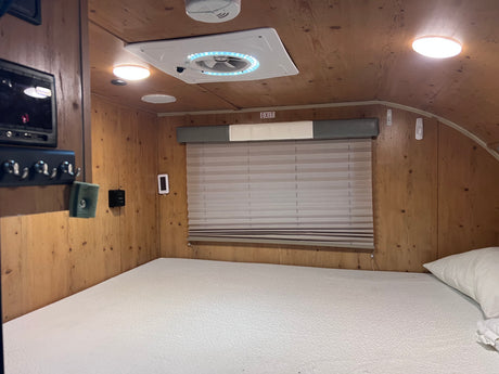 Experience comfort in this RV rental bedroom: wood-paneled walls, cozy bed, bright ceiling fan, and window blinds.