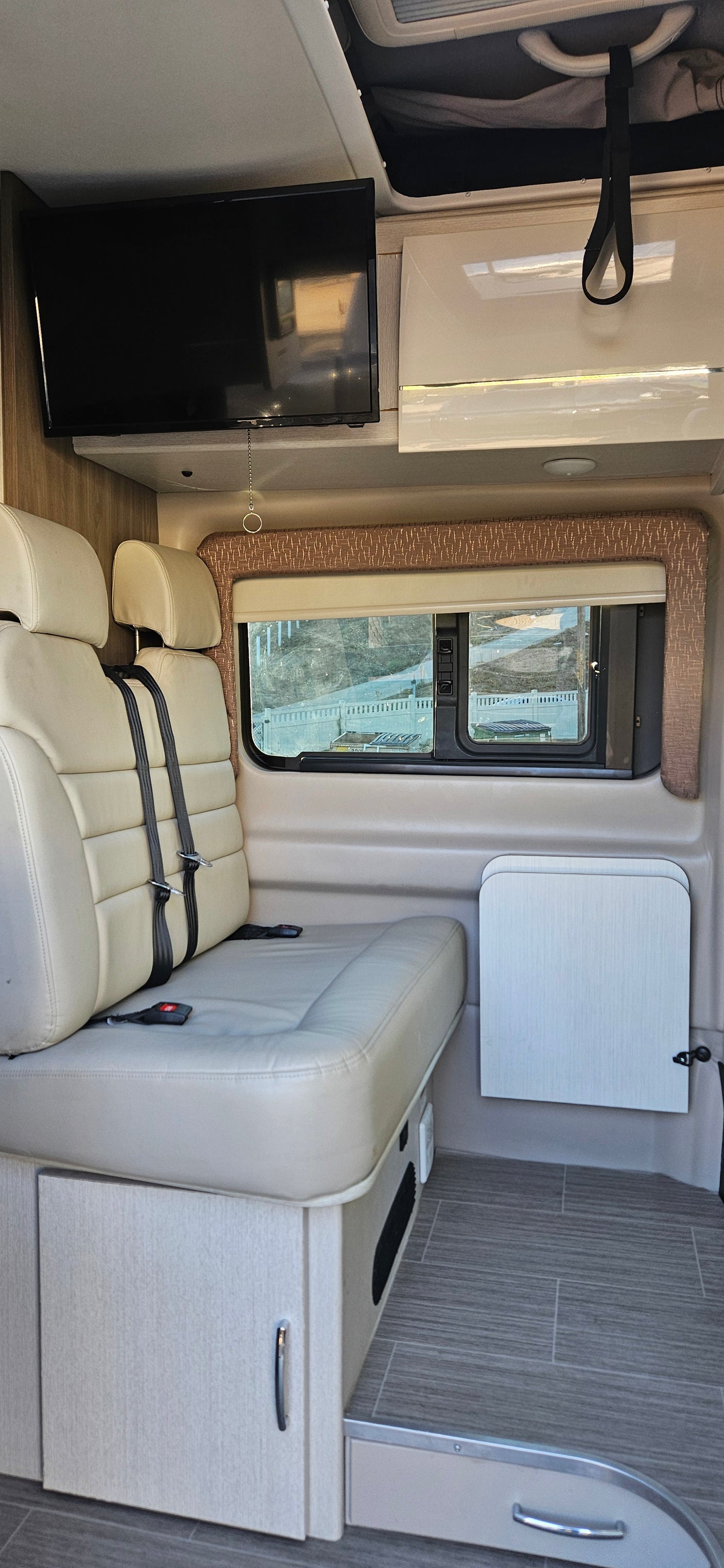 Inside an RV rental: a modern interior with plush bench seating, mounted TV, window views, and a wall-mounted table.