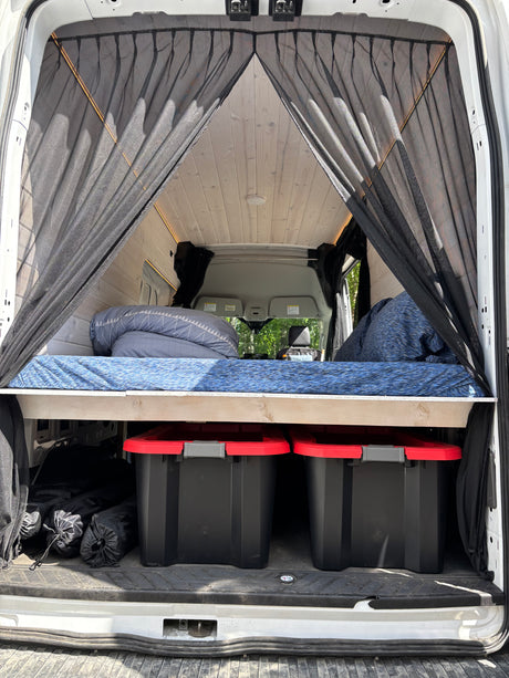 RV rental: Inside a camper van conversion with a raised bed, under-bed storage bins, and rear insect netting.