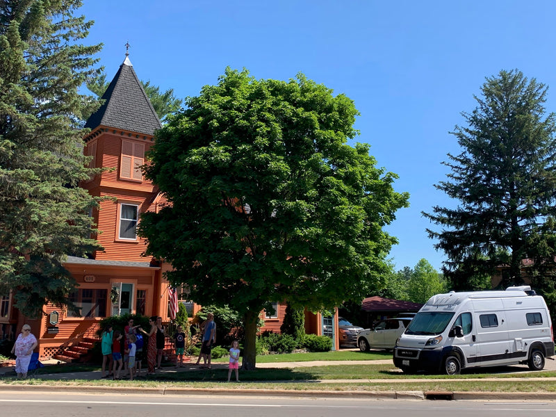 People gathered near a unique orange house with a turret and a white RV rental van parked curbside on a sunny day. — photo 20