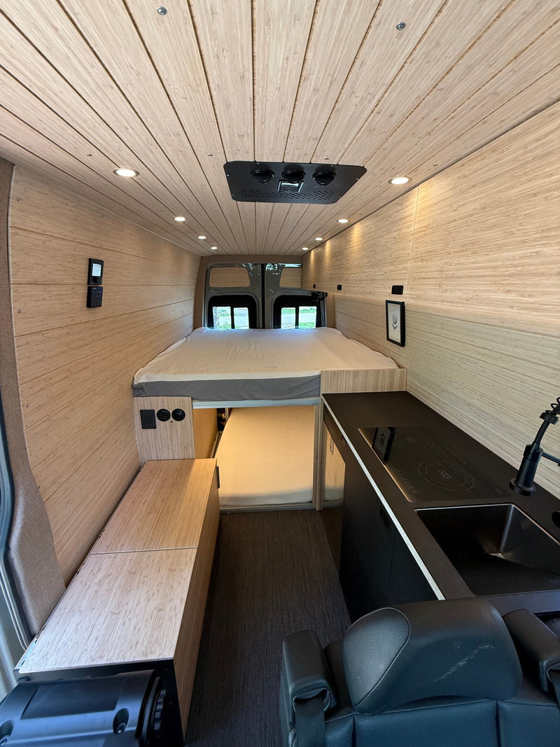 Modern rv rental interior with bamboo paneling, large bed, and compact kitchen for comfortable travel. — photo 11