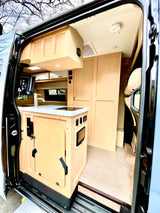 Detailed view of an rv rental's interior: modern kitchen with sink/stove, TV, light wood cabinets, and tiled floor.