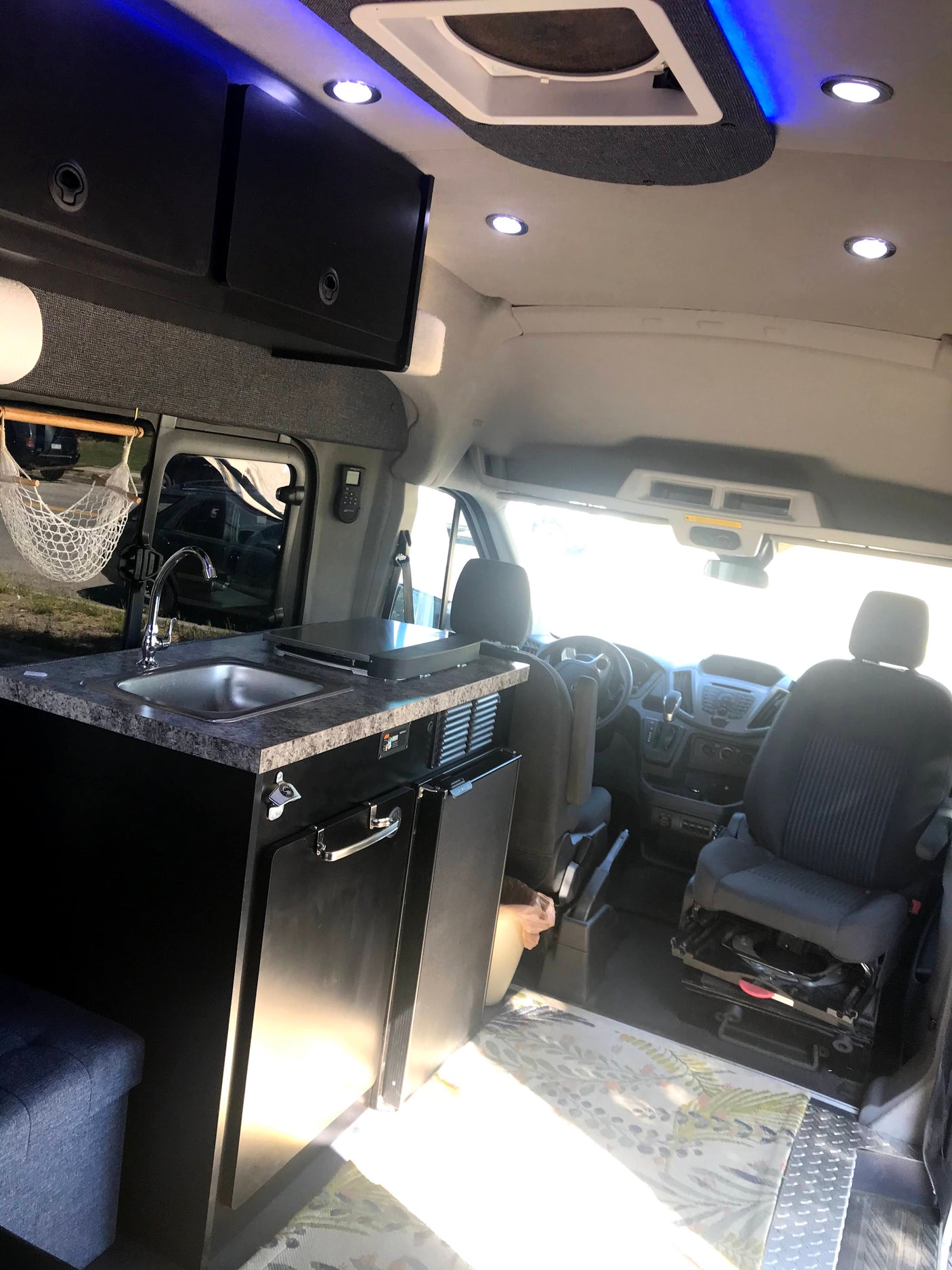 Inside this custom RV rental, discover a compact camper kitchen with sink, grill, and driver's cabin area.