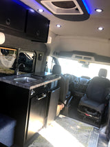 Inside this custom RV rental, discover a compact camper kitchen with sink, grill, and driver's cabin area.
