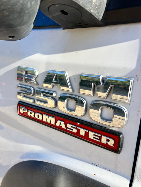 Close-up of a chrome 'RAM 2500 PROMASTER' emblem on a white van, often seen as an rv rental conversion.