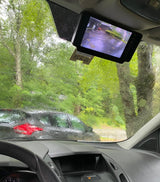 Rainy RV rental day: View from inside, raindrops on windshield, showing trees, a car, and a backup camera monitor.