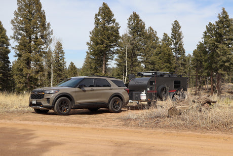 Adventure-ready Ford Explorer and overland trailer rv rental parked on a dirt road amidst pine trees, perfect for camping.