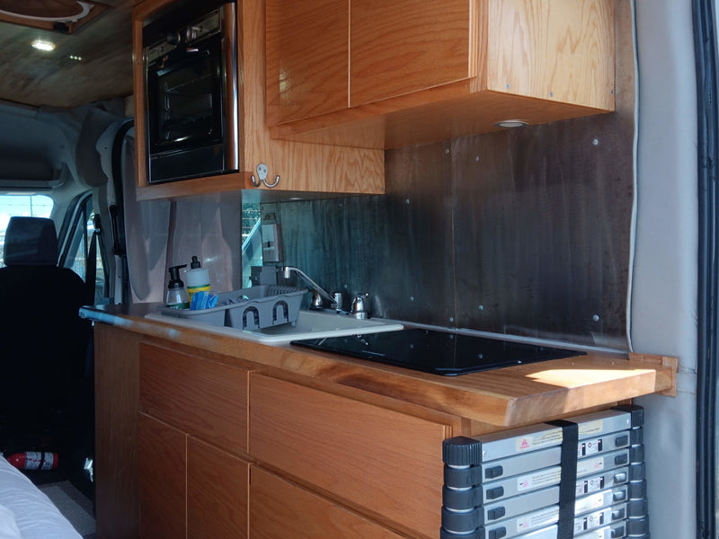 Inside an RV rental, a compact kitchen with warm wood cabinetry, built-in microwave, sink, and stove. Ready for adventures! — photo 9
