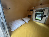 Inside this cozy RV rental, a compact sleeping area features a bed with patterned pillows against warm wood paneling.