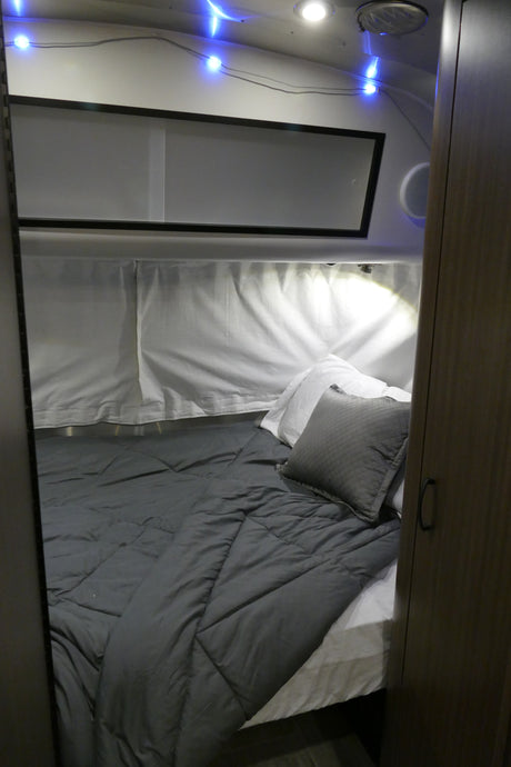 Cozy RV rental bedroom featuring a gray comforter, white pillows, blue string lights, and a bright reading lamp.
