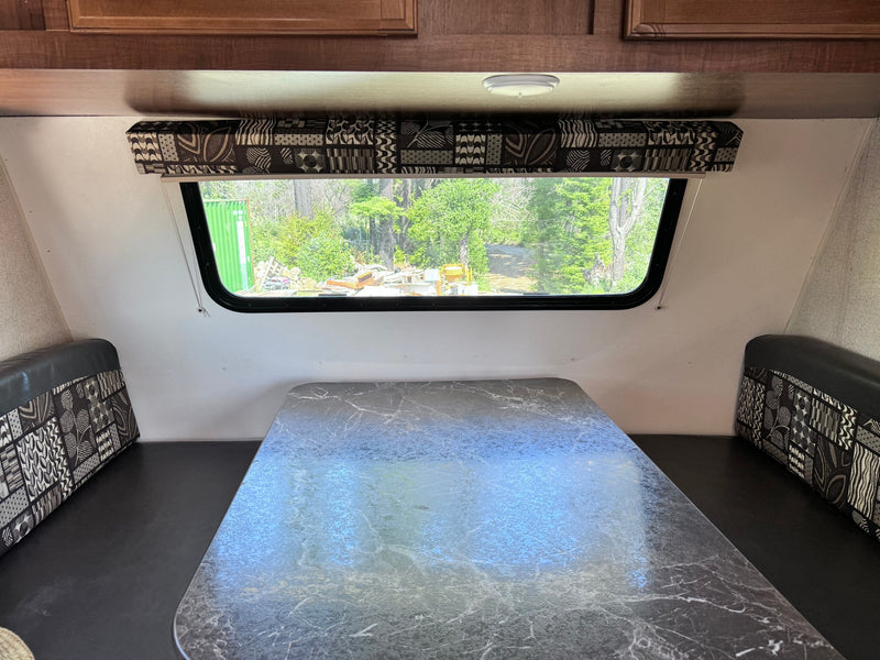 RV rental interior: A dinette area with a marbled table, patterned bench cushions, and a large window overlooking trees. — photo 9