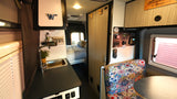 Spacious RV rental interior showcasing a kitchenette, dinette, controls panel, and a cozy bed area for comfortable travel.