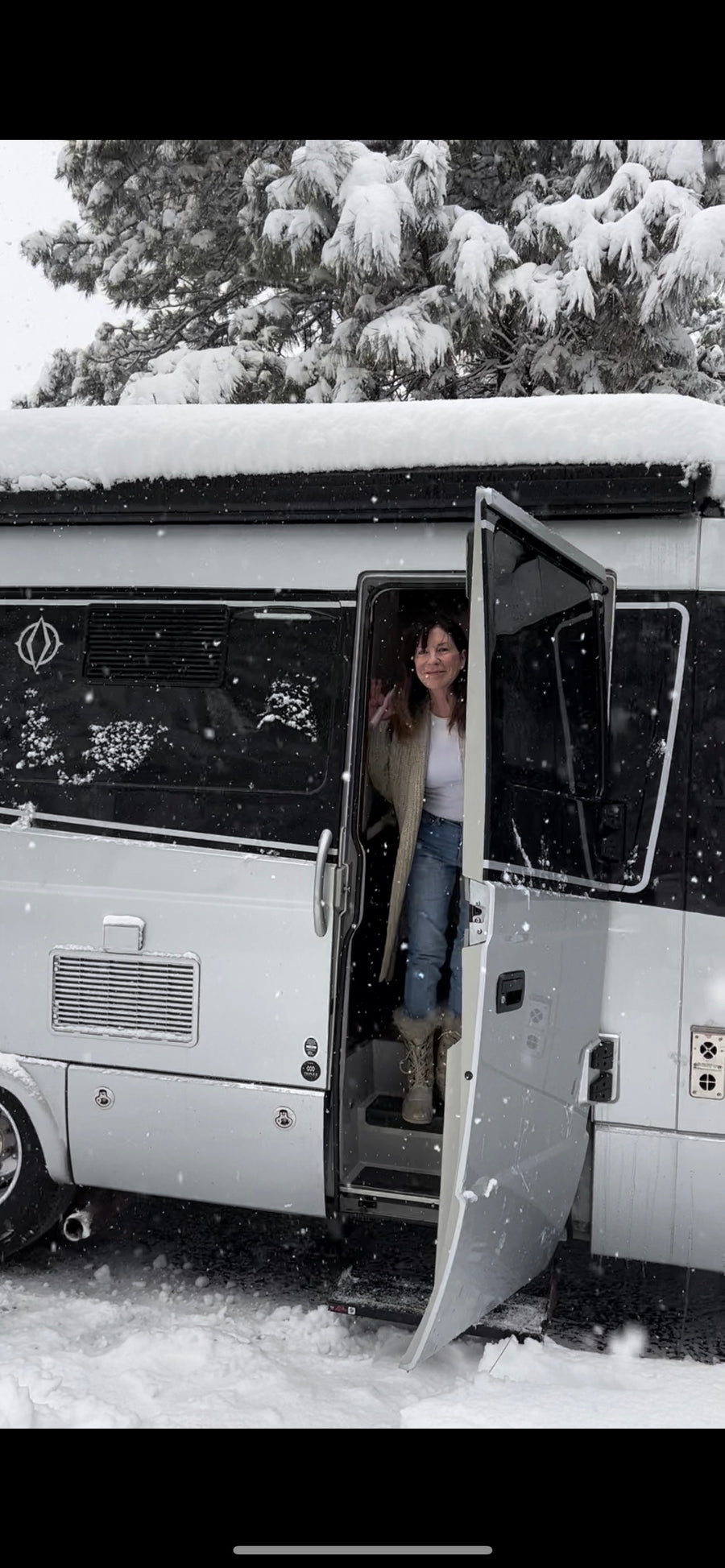 Woman smiles from her RV rental doorway, surrounded by snow & pines. Perfect winter motorhome adventure!