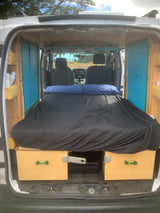 Camper van interior for your next RV rental. Shows a comfy black bed, custom wood storage, and front cabin view.