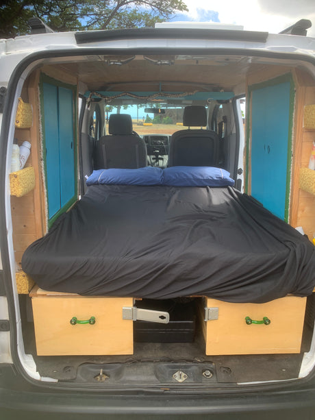 Camper van interior for your next RV rental. Shows a comfy black bed, custom wood storage, and front cabin view.
