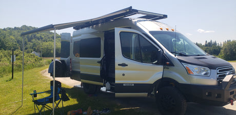 Rugged silver Ford Transit 4x4 camper van with awning & gear set up, ideal for your RV rental adventure.