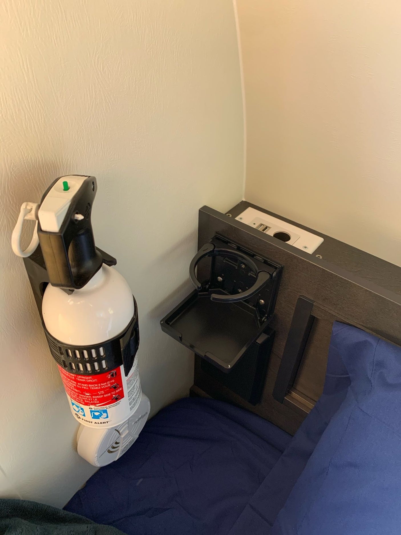 RV rental safety: A mounted fire extinguisher and bedside charging/cupholder setup for a compact bedroom.
