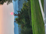 Striking pink sun sets over serene blue mountains and vibrant green trees, alongside a grassy path. Explore this beauty with an RV rental.