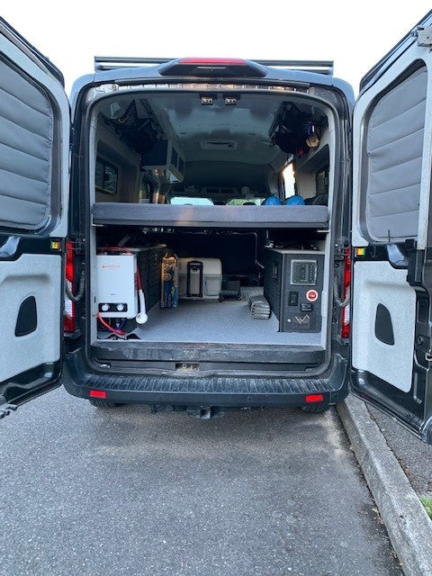 Inside an RV rental: a camper van's open rear reveals smart storage, a cozy bed platform, and a portable shower system.