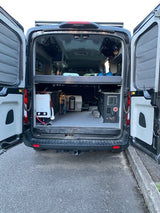 Inside an RV rental: a camper van's open rear reveals smart storage, a cozy bed platform, and a portable shower system.