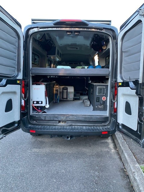 Inside an RV rental: a camper van's open rear reveals smart storage, a cozy bed platform, and a portable shower system.