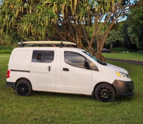 This white camper van, equipped with a surfboard on its roof rack, is ready for your next RV rental camping adventure in nature.