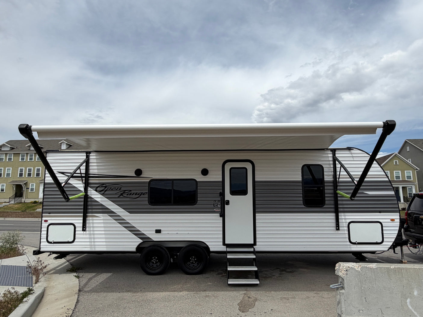 A white and gray Open Range travel trailer rv rental, with an extended awning, parked outside under a cloudy sky.