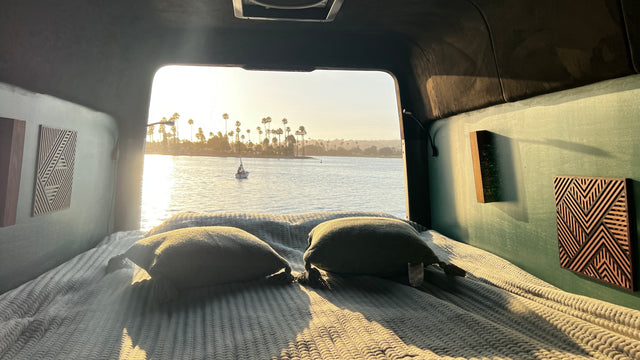 Cozy RV rental bed with a stunning water view. Enjoy serene sunsets, sailboats, and palm trees from your van life retreat.