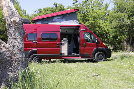 Red pop-top RV rental, an ideal camper van for exploring nature, parked by a tree in a sunny field.