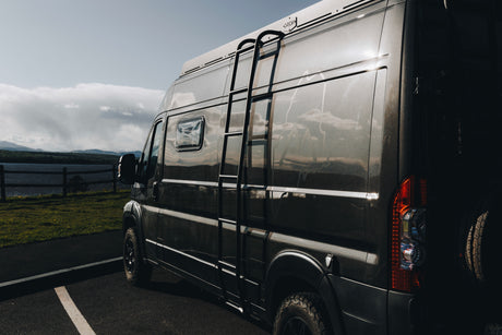Dark grey camper van, an ideal rv rental, parked by a scenic lake, inviting adventure and outdoor exploration.