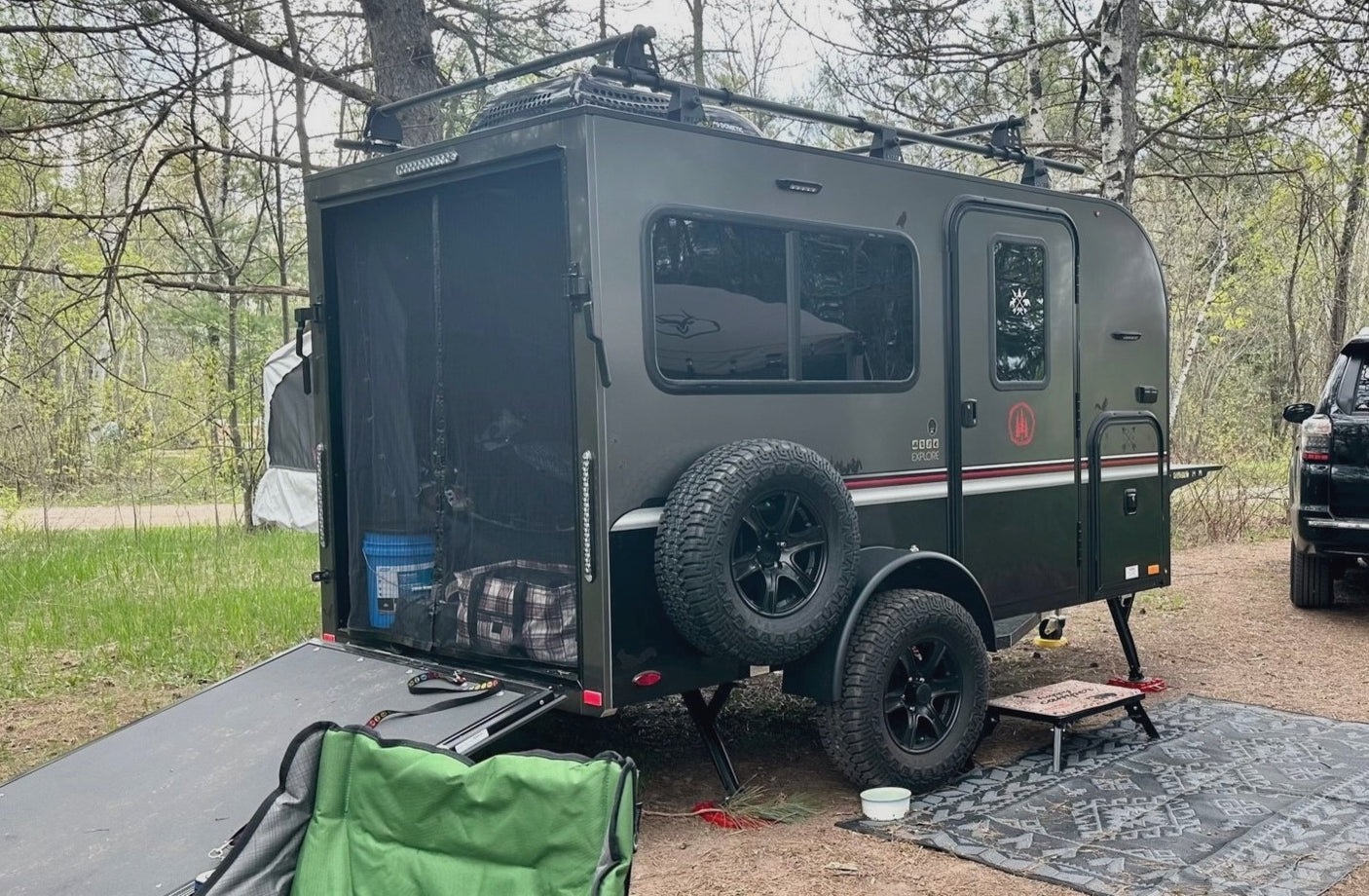 Off-road CEDA EXPLORE camper trailer RV rental with rear ramp down, set up for camping in a wooded outdoor site.