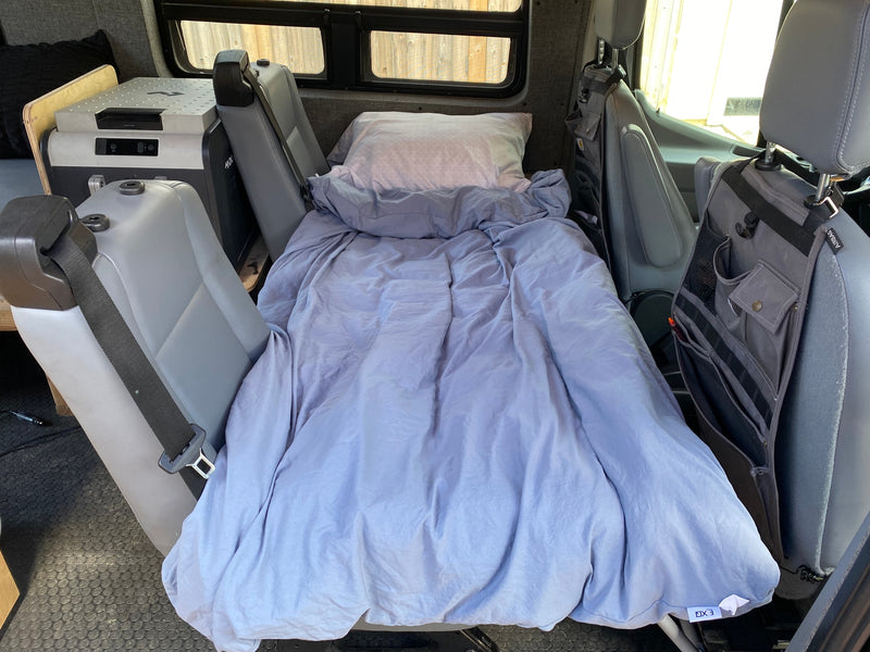 An RV rental's compact sleeping area features a bed with purple bedding, a portable cooler, and headrest storage. — photo 11