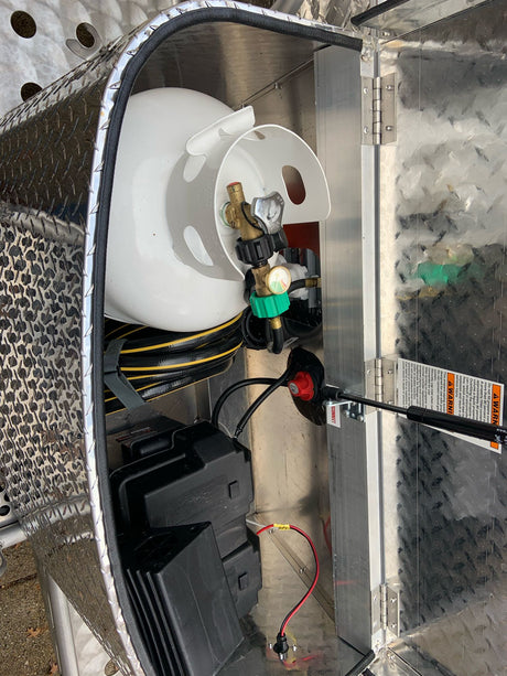 An RV rental's utility compartment with a propane tank, batteries, and hose, all in a durable diamond plate interior.