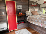 Cozy RV rental interior: wood-paneled walls, "Happy Camper" bed, fun decor, and practical camping amenities.