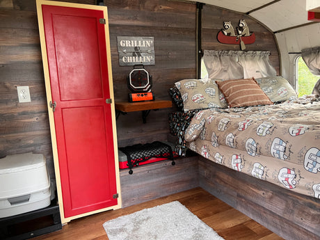 Cozy RV rental interior: wood-paneled walls, "Happy Camper" bed, fun decor, and practical camping amenities.
