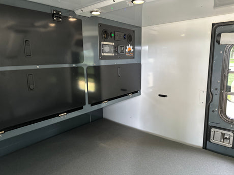 Inside an RV rental: off-grid trailer with integrated control panel, overhead lighting, and storage.